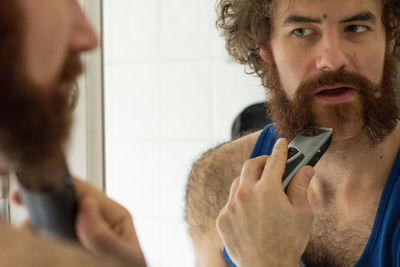 Reflection of man trimming beard on bathroom mirror