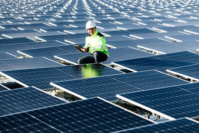 Asian engineer on background field of photovoltaic solar panels solar cells on roof top factory.