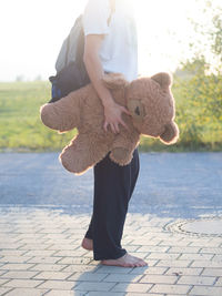 Low section of man holding teddy bear on footpath