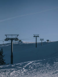 Electricity pylon on snow covered landscape against sky