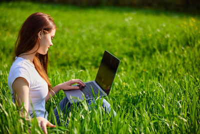 Young woman using laptop while sitting on grassy field