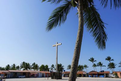 Low angle view of palm tree by cross against clear sky