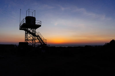 Silhouette tower on field against sky during sunset