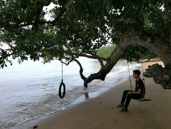 Full length of man sitting on swing at beach