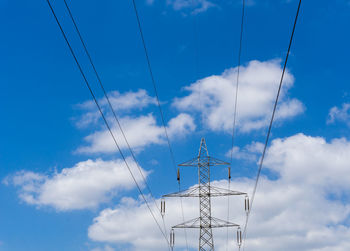 Low angle view of electricity pylon against blue sky