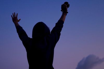 Low angle view of person with arms raised standing against sky at dusk