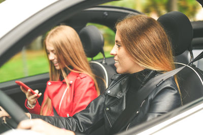 Trendy girls sitting in a convertible car. smiling teen driving with friend beside using smartphone