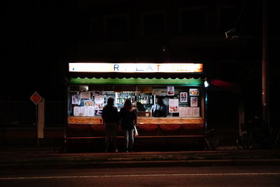Rear view of people walking on illuminated street at night