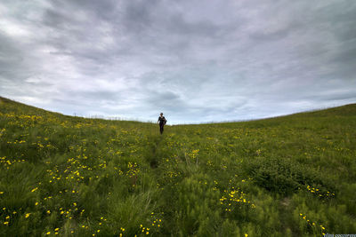 Woman standing on grassy field against cloudy sky