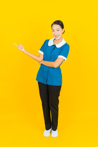 Portrait of young woman standing against yellow background