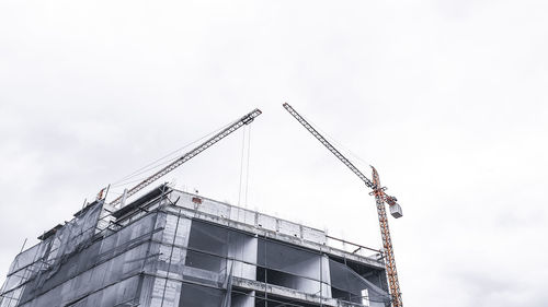 Low angle view of crane at construction site against sky