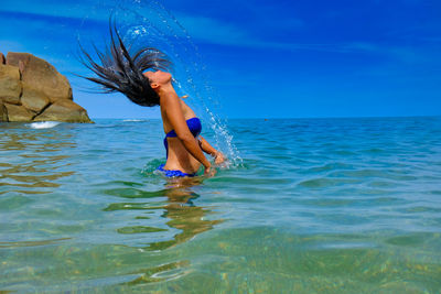 Woman tossing hair in sea against blue sky