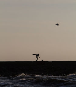 Silhouette person standing in sea against sky during sunset