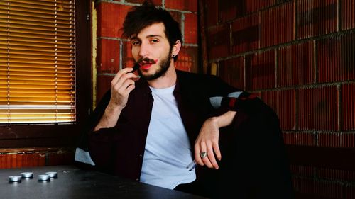 Portrait of young man applying lipstick while sitting at home