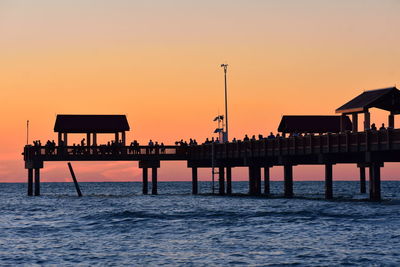 Silhouette pier on sea against orange sky