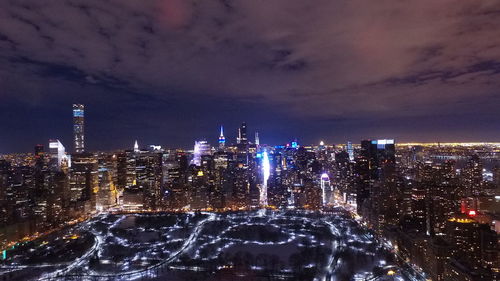 Illuminated buildings against cloudy sky at night