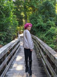 Portrait of woman standing on footbridge amidst forest