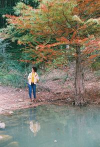 Full length of woman standing by lake in forest