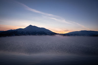Mist rising above wintry bay water with mountains and sunset. panoramic view.