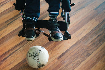 Low section of person sitting on wheelchair by soccer ball at home