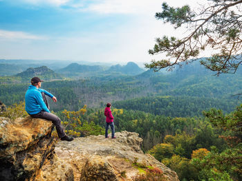 Man hiker sit on edge and woman tourist watching over sunny natural landscape. saxon switzerland