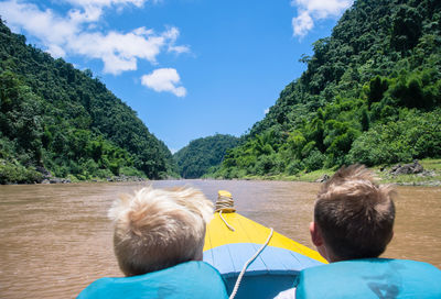 Rear view of boys in boat on lake by mountains against sky