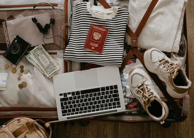 Open baggage with snickers, sweater, laptop, headphones and passport, vintage camera and backpack.