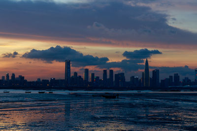 Sea by modern buildings against sky during sunset