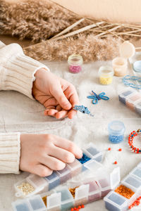 The girl's hands are weaving a dolphin on a table with items for beading. 