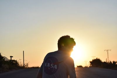 Rear view of man standing on road against sky during sunset