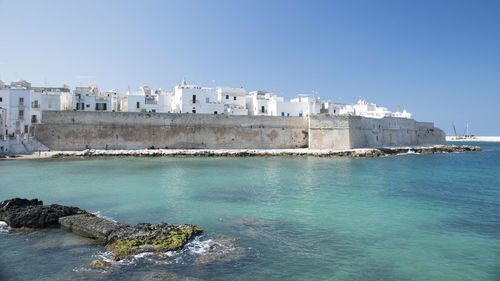 View of buildings in front of sea against clear blue sky