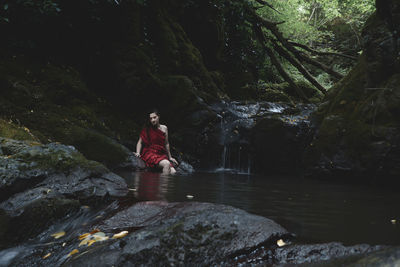 Woman sitting by stream in forest