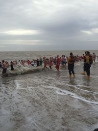 People on beach against cloudy sky