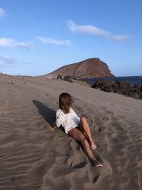 Woman sitting on beach against sky