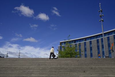 Rear view of woman walking on staircase against sky