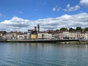 Buildings at waterfront against cloudy sky