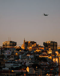 Airplane flying over buildings in city against clear sky