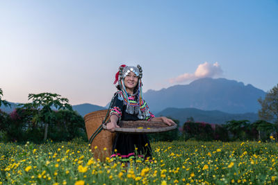 Smiling woman in traditional clothing holding wicker basket while standing in farm