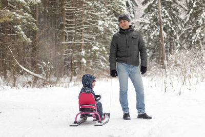 Full length of father with son standing on snow covered land during winter