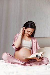 Pregnant woman writing on bed at home