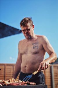 Shirtless man grilling food outdoors