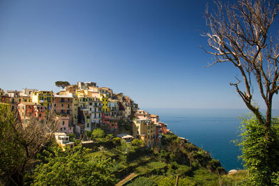Buildings by sea against clear blue sky