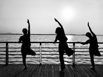 Silhouette female friends exercising on pier over sea against sky