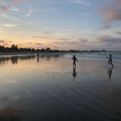 Silhouette childrens on beach against sky during sunset