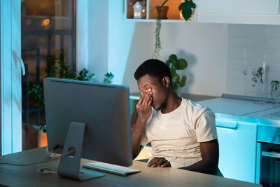 Overworked african man freelancer feeling eye strain and fatigue during prolonged computer use