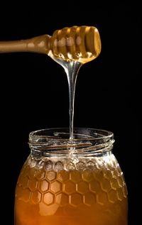 Close-up of dipper pouring honey in jar against black background