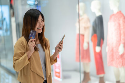 Young woman using phone while standing on laptop