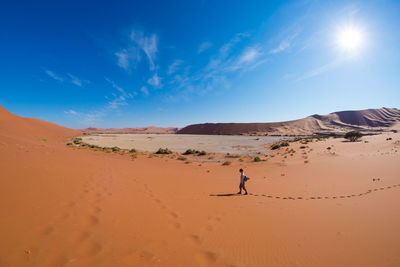 Tourist walking in desert at namib-naukluft national park against sky during sunny day