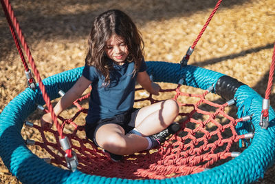 Portrait of a beautiful caucasian girl sits on a round rope swing in the park at the playground