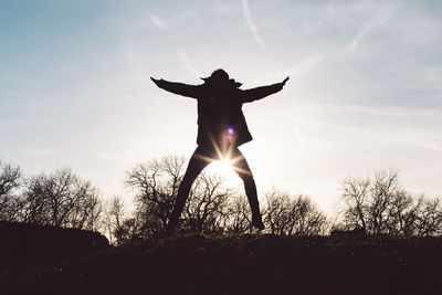 Silhouette man with arms outstretched on field against sky